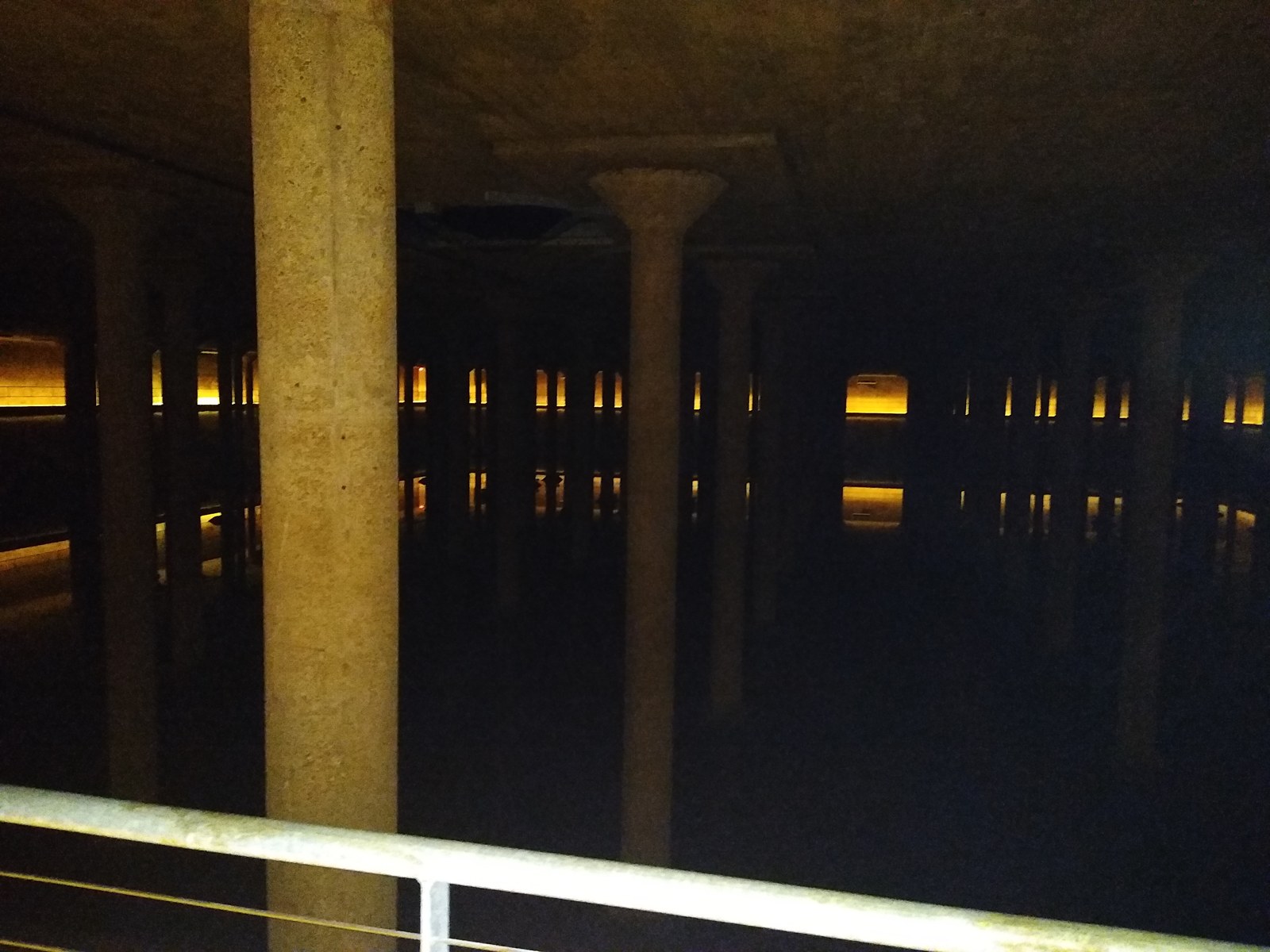 Another view across the concrete columns of Buffalo Bayou Park Cistern, with a visitor railing in the foreground.