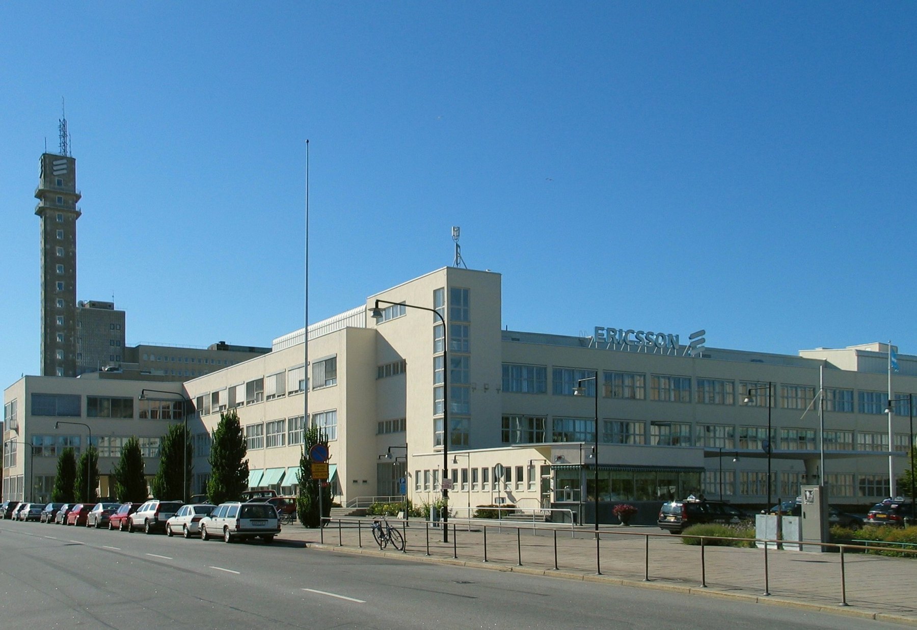 Daylight view of the Ericsson buildings at Telefonplan, with an unlit narrow tower on the left and a blue sky above.